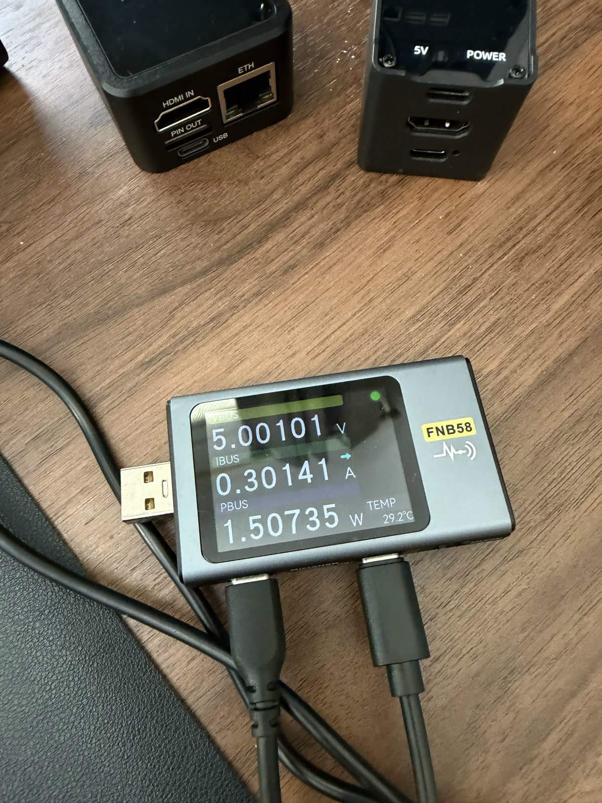 The FNIRSI meter inline on a KVM's power feed, logging the streaming draw we report in the power comparison.